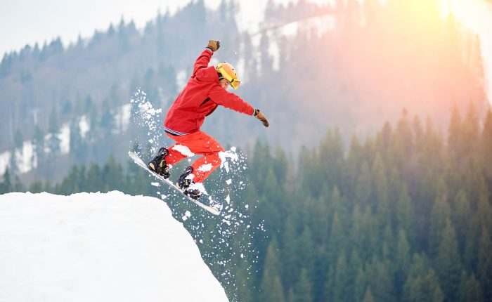 Male snowboarder freerider jumping from the top of the snowy hill with snowboard. Skiing and snowboarding concept